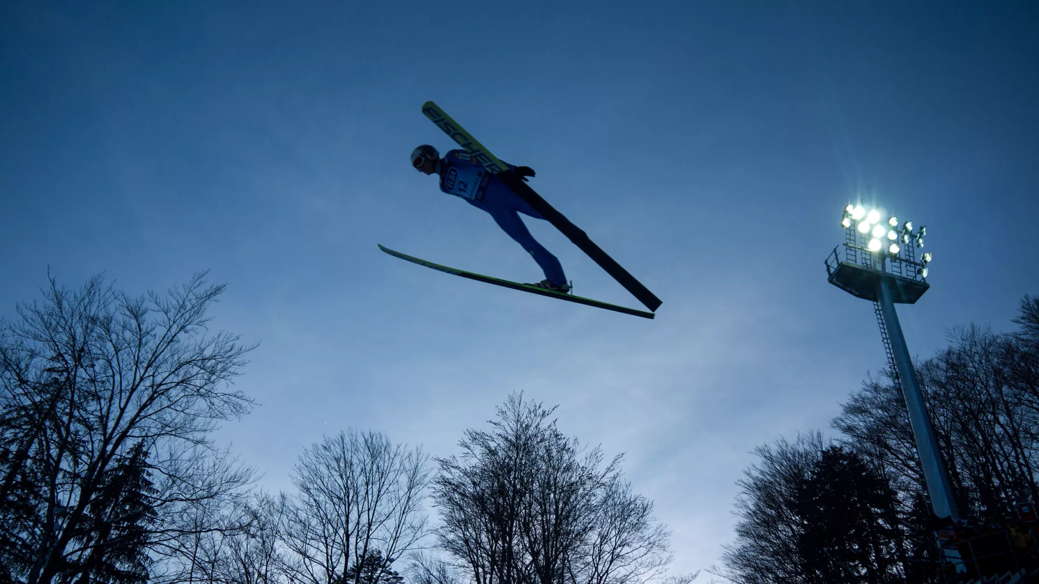 Skispringer im Flug vor einem Flutlichtmast der Skiflugschanze Oberstdorf